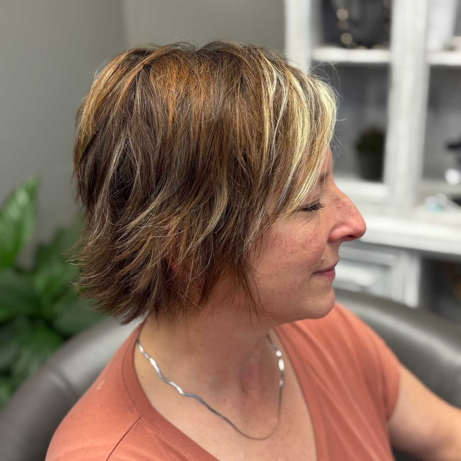 Short-haired woman in profile sitting on a couch, wearing a peach top.